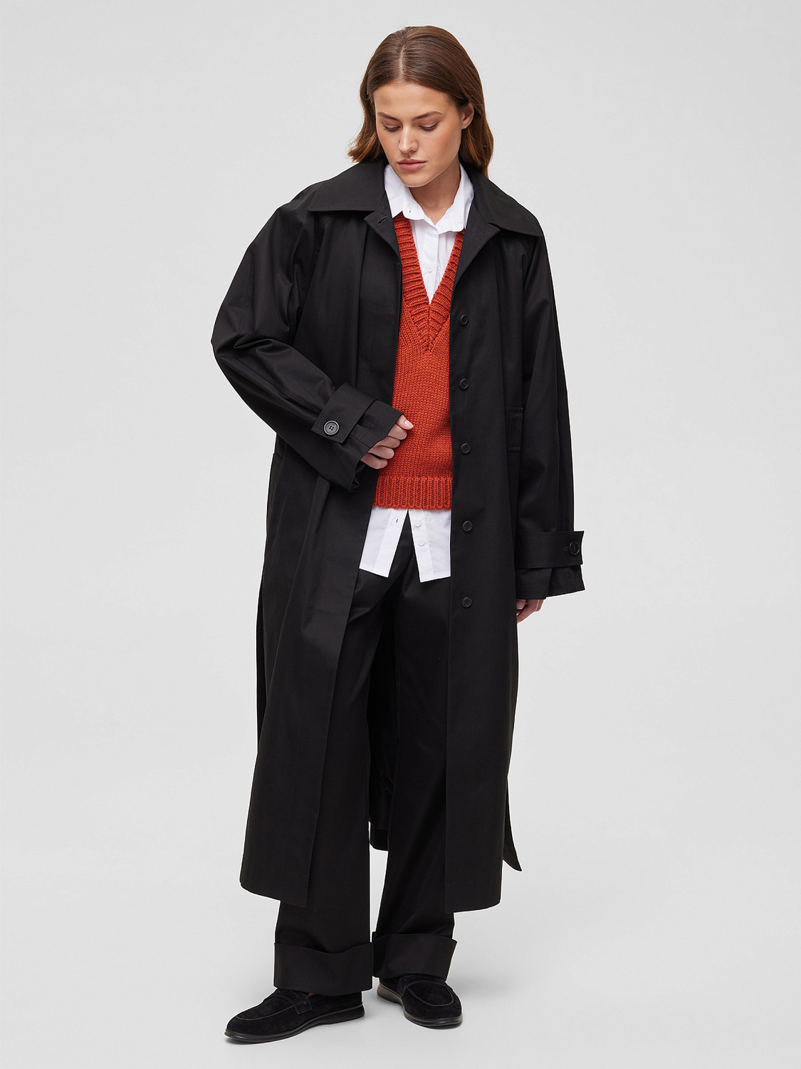 Woman in black trench coat layered with sweater vest